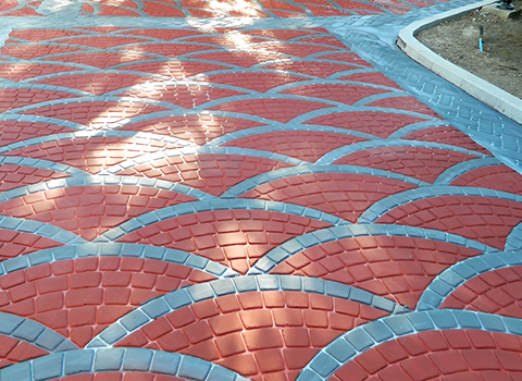 Red interlocking paving stones with blue curved joints forming a decorative repeating arc pattern over a walkway.