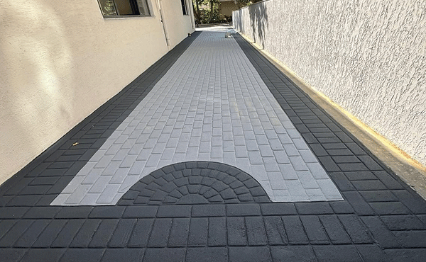 Long paved walkway between beige walls, with a light gray central path and a semicircular brick pattern at the near end.